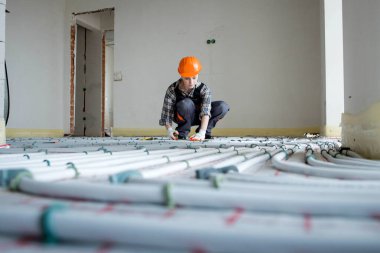 A female construction worker checks the installation of a warm floor with a tape measure at the construction site