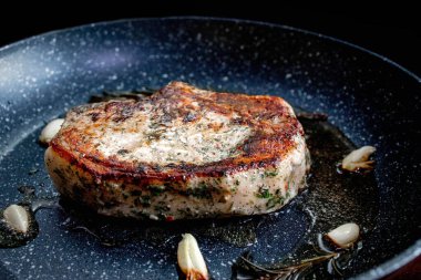 Grilled premium rib eye beef steak in the pan, cooking steak in the kitchen on a dark background. Overhead shot of chef preparing ribeye with butter, thyme and garlic
