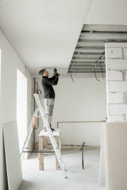 İşçi metal çerçeveye alçı yapıştırıyor. Tavan kurulumu.