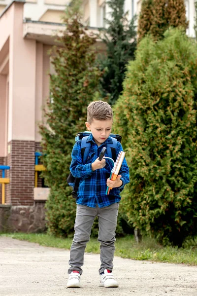 小一年级学生背着背包看那本抄本 放学回家 — 图库照片