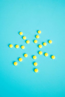 Mavi arka plandaki bir şişeden çıkan sarı haplardan oluşan bir güneş.