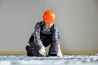 A female construction worker checks the installation of a warm floor with a tape measure at the construction site