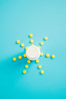 Mavi arka planda sarı haplardan ve şişeden bir güneş..