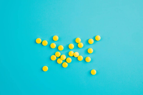 Chaotically arranged yellow pills on a blue background, healthy and medicine concept.