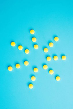 Mavi arka plandaki bir şişeden çıkan sarı haplardan oluşan bir güneş.