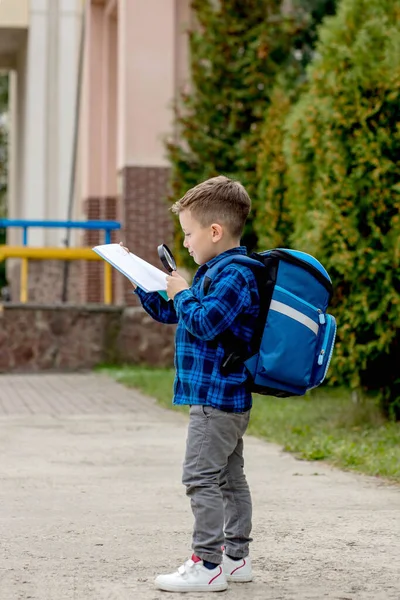 一个小男孩透过放大镜向教科书望去 幼儿的教育 回到学校的概念 — 图库照片