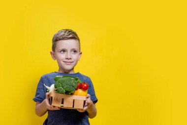 Sarı arka planda taze ananas, elma ve portakal tutan gülümseyen çocuğun stüdyo fotoğrafı. Sağlıklı bebek maması konsepti.