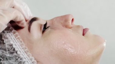 Kozmetik uzmanı maskeyi nazikçe kadının yüzünün derisine uyguluyor. Deriyi kirlilikten arındırıyor. Deri temizleme, gençleştirme, sivilce tedavisi. Bakım prosedürleri