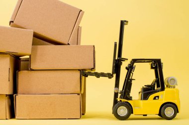 Forklift kamyonu sarı arka planda karton kutular kaldırıyor. Kargo sıralama kavramı.