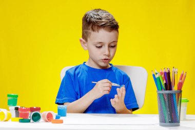 Küçük bir anaokulu öğrencisi elinde fırçayla masada oturur ve avucunu boyar. Anaokulu geliştirme