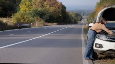 Bozuk bir arabanın yanında duran genç bir kadın sürücü kaputunu açtı ve kötü cep telefonu şebekesinden çağrı almak için aradı..