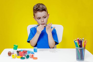 Küçük bir anaokulu öğrencisi elinde fırçayla masada oturur ve avucunu boyar. Anaokulu geliştirme