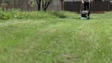 Evinin arka bahçesinde çim biçen bir adam. Çim biçme makinesi olan adam.