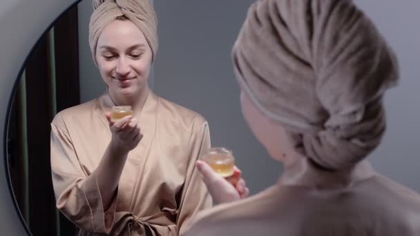 Retrato Mulher Roupão Banho Com Toalha Cabeça Aplica Creme Rosto — Vídeo de Stock