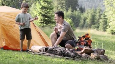 Mutlu baba ve oğul kamp alanında marşmelov kızartıyorlar. Yürüyüş, aileyle zaman geçirmek, aile hayatı, açık hava eğlencesi.