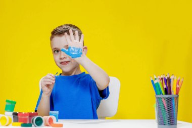 Küçük bir anaokulu öğrencisi elinde fırçayla masada oturur ve avucunu boyar. Anaokulu geliştirme