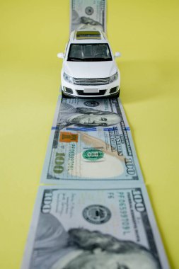 Oyuncak araba sarı arka planda Amerikan kağıt para yolunda ilerliyor.