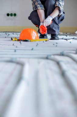 Sıkı bir şapka, kerpeten ve sıcak zeminde eldiven tamir etmek için aletlerin yanında çalışan bir işçi. Sıcak bir zemin kurulumu.