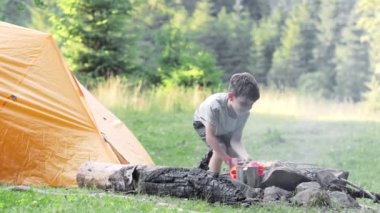 Doğada barbekü yapan bir çocuk. Terbiye edilmiş et kömürde kızartılır. Çadırın yanında barbekü hazırlama süreci