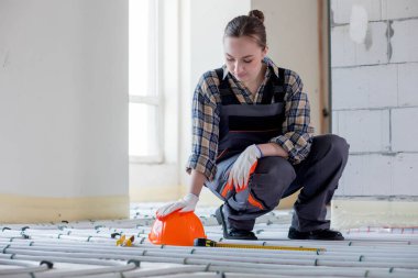 Sıkı bir şapka, kerpeten ve sıcak zeminde eldiven tamir etmek için aletlerin yanında çalışan bir işçi. Sıcak bir zemin kurulumu.