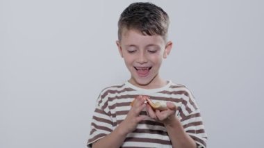 Küçük çocuk lezzetli bir şekilde gri arka planda salamlı pizza yiyor..