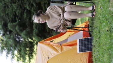 Kadın telefonu güneş paneli enerjisiyle şarj ediyor. Kamp yapmak için temiz enerji ya da elektrik olmadığı zaman evde kullanmak için.