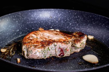 Grilled premium rib eye beef steak in the pan, cooking steak in the kitchen on a dark background. Overhead shot of chef preparing ribeye with butter, thyme and garlic