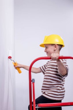Boyalı silindirli şirin bir çocuk. Mutlu çocuk ebeveynlerin duvar boyamasına yardım eder. Aile için yeni bir ev