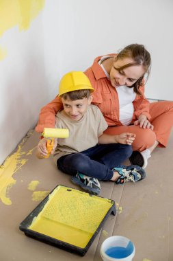 Ev tamiri. Anne oğluna bir silindirle duvarı boyamasında yardım ediyor. Çocuk dairenin duvarını boyuyor. Yeni ev yenileme konsepti