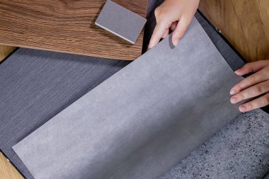 Bir iç mimarın eli, farklı türde yapay taş, doku ve renkleri, ahşap MDF tahtası ve dekoratif duvar kağıdı içeren bir palet seçer..