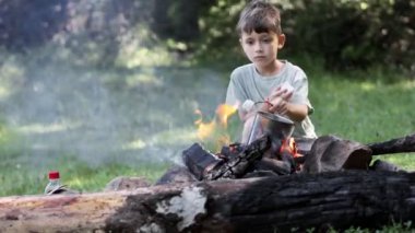 Şenlik ateşinin yanında oturan küçük çocuk çubuk düşüşünde lokum pişiriyor..