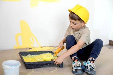 Boyalı silindirli şirin bir çocuk. Mutlu çocuk ebeveynlerin duvar boyamasına yardım eder. Aile için yeni bir ev