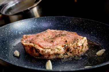 Şef, biberiye ve sarımsaklı tavada sulu et pişiriyor, mutfak gereçleri kullanıyor. Kızarmış biftek pişirme işlemi