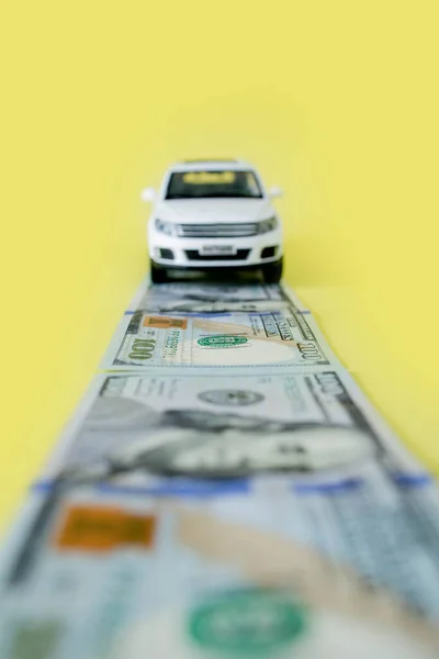 Toy car moving on a US paper currency road on yellow background