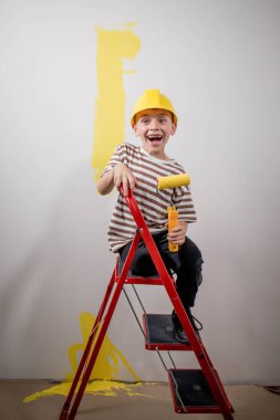 Çocuk bir silindirle bir duvar boyuyor. Çocuk büyük bir boya fırçası tutuyor. Ev onarımı