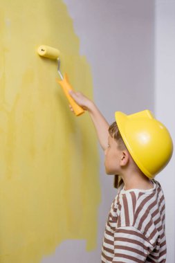 Boyalı silindirli şirin bir çocuk. Mutlu çocuk ebeveynlerin duvar boyamasına yardım eder. Aile için yeni bir ev