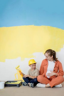 Ev tamiri. Anne oğluna bir silindirle duvarı boyamasında yardım ediyor. Çocuk dairenin duvarını boyuyor. Yeni ev yenileme konsepti