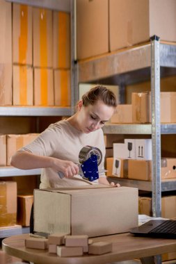 Gülümseyen bayan girişimci bant kutusunu kullanarak paketliyor. Kadın, ürün kutusunu müşteriye teslim etmek için hazırlıyor. Çevrimiçi iş, ekommerce ve dağıtım kavramı.