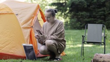 Kadın telefonu güneş paneli enerjisiyle şarj ediyor. Kamp yapmak için temiz enerji ya da elektrik olmadığı zaman evde kullanmak için.