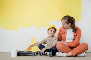 Ev tamiri. Anne oğluna bir silindirle duvarı boyamasında yardım ediyor. Çocuk dairenin duvarını boyuyor. Yeni ev yenileme konsepti