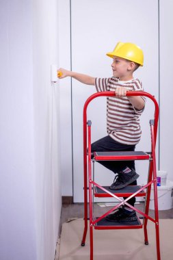 Boyalı silindirli şirin bir çocuk. Mutlu çocuk ebeveynlerin duvar boyamasına yardım eder. Ev yenilenmesi.