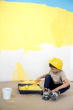 İnşaat üniformalı bir çocuk boyaların yanında oturuyor. Onarım. Duvarları boyuyorum..