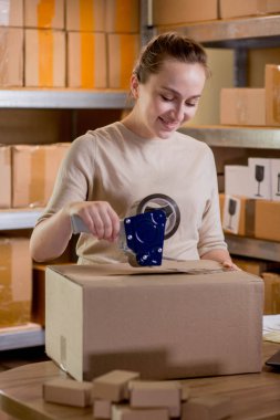 Gülümseyen bayan girişimci bant kutusunu kullanarak paketliyor. Kadın, ürün kutusunu müşteriye teslim etmek için hazırlıyor. Çevrimiçi iş, ekommerce ve dağıtım kavramı.