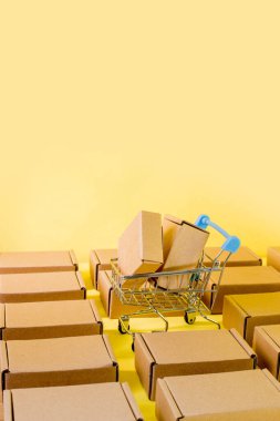 Alışveriş konsepti: Sarı arka planda mavi arabalı kutular. Çevrimiçi alışveriş tüketicileri ev ve dağıtım hizmetlerinden satın alabilirler. Kopyalama alanı ile.