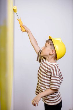 Boyalı silindirli şirin bir çocuk. Mutlu çocuk ebeveynlerin duvar boyamasına yardım eder. Aile için yeni bir ev