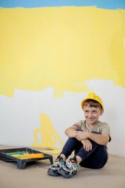 Boyalı silindirli şirin bir çocuk. Mutlu çocuk ebeveynlerin duvar boyamasına yardım eder. Aile için yeni bir ev