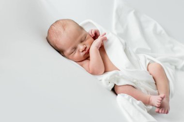 Beyaz bir örtüye sarılmış, beyaz bir arka planda uyuyan 3 günlük bir bebek..