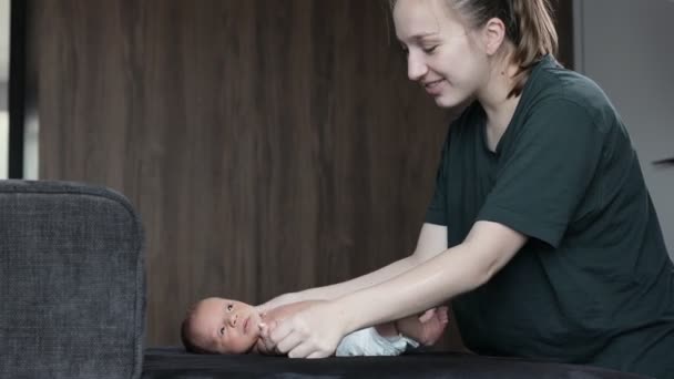 妈妈和一个新生婴儿一起做体操 这个婴儿躺在一个黑色的沙发上 — 图库视频影像