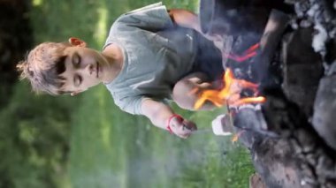 Şenlik ateşinin yanında oturan küçük çocuk çubuk düşüşünde lokum pişiriyor.
