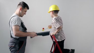 Baba ve oğlu evlerinin bir odasına sarı boyalı bir duvar boyuyorlar..
